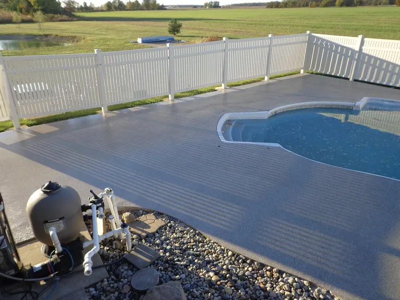 Gray coated pool deck by a vinyl fence